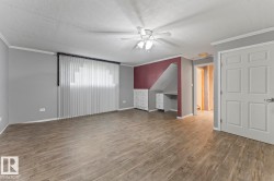 Spacious room featuring wood-finish flooring, a ceiling fan with integrated lighting, and a built-in desk with cabinetry - 