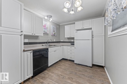 Kitchen featuring white cabinetry, wood-finish flooring, a stainless steel sink, and a black dishwasher - 4412 51 Avenue, Cold Lake, AB - Indoor Photo Showing Kitchen With Double Sink