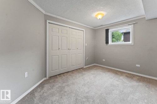 Carpeted room featuring a double bi-fold closet, a single window, overhead lighting, and crown molding - 4412 51 Avenue, Cold Lake, AB - Indoor Photo Showing Other Room