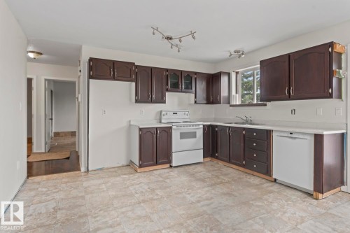 Spacious kitchen featuring dark wood cabinetry, light-toned countertops, and a full suite of white appliances including a range and dishwasher - 4412 51 Avenue, Cold Lake, AB - Indoor Photo Showing Kitchen