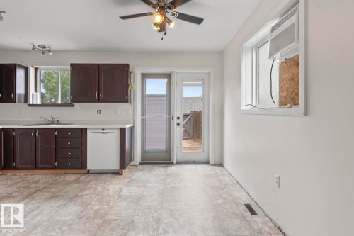 Kitchen area with dark wood-finish cabinetry, light-toned countertops, and a white dishwasher - 4412 51 Avenue, Cold Lake, AB - Indoor Photo Showing Kitchen