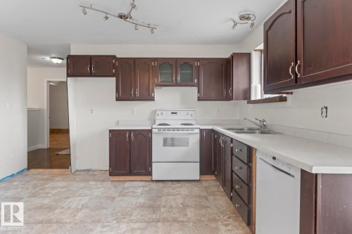 Kitchen featuring dark wood-finish cabinetry, white countertops, and tile flooring - 4412 51 Avenue, Cold Lake, AB - Indoor Photo Showing Kitchen With Double Sink