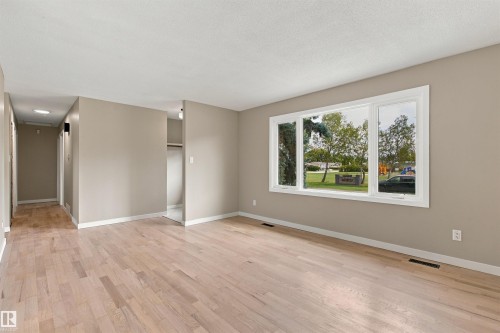 Wide window with white trim, light tone wood-finish flooring, and neutral wall paint - 9908 99 Street, Morinville, AB 