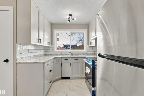 Contemporary kitchen featuring white cabinetry, black hardware, a stainless steel sink, a subway tile backsplash, and light-toned countertops - 9908 99 Street, Morinville, AB 