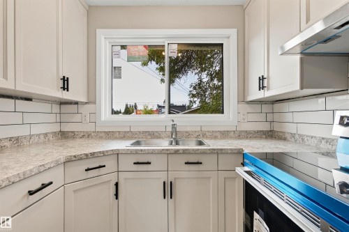 White cabinetry with dark hardware, subway tile backsplash, stainless steel appliances, durable countertops, and a ceiling-mounted light fixture - 9908 99 Street, Morinville, AB 