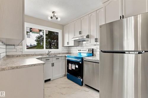 Kitchen featuring white shaker cabinetry, white subway tile backsplash, light-toned countertops, a stainless steel refrigerator, and a built-in range - 9908 99 Street, Morinville, AB 