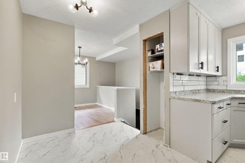 White shaker cabinetry, light-toned countertops, white subway tile backsplash, white tile flooring, and wood-finish flooring - 9908 99 Street, Morinville, AB 