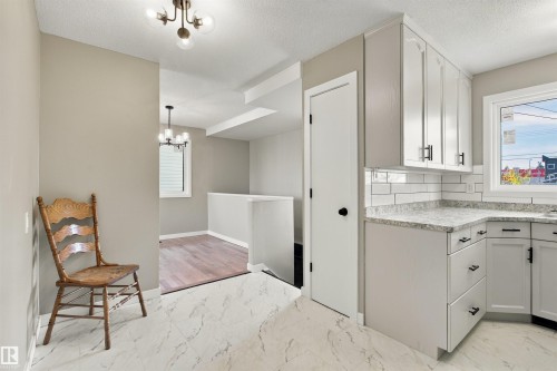 Light wood-finish flooring, recessed kitchen with stainless steel refrigerator, white tile backsplash, contemporary black chandelier, and multi-pane window - 9908 99 Street, Morinville, AB 