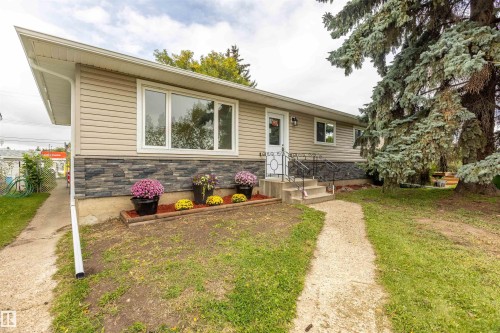 Siding exterior with a stone veneer accent, white-trimmed windows, and a concrete pathway leading to the front entry - 9908 99 Street, Morinville, AB 