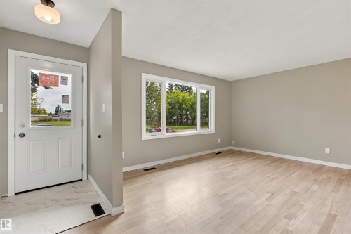 Recessed lighting, wood-finish flooring, neutral wall tones, large window, and a paneled entry door - 9908 99 Street, Morinville, AB 