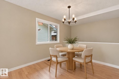 Light wood-finish flooring, half-wall partition, white trim accents, and a contemporary dark bronze chandelier - 9908 99 Street, Morinville, AB 