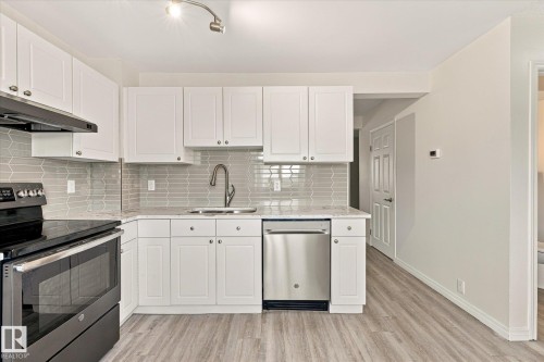 White cabinetry, stainless steel appliances, patterned tile backsplash, light-toned wood-finish flooring, and track lighting - #3 18010 98 Av Nw, Edmonton, AB 