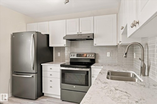 White shaker cabinetry, stainless steel appliances, patterned tile backsplash, single basin sink, and wood-finish flooring - #3 18010 98 Av Nw, Edmonton, AB 