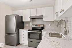 White shaker cabinetry, stainless steel appliances, patterned tile backsplash, single basin sink, and wood-finish flooring - 