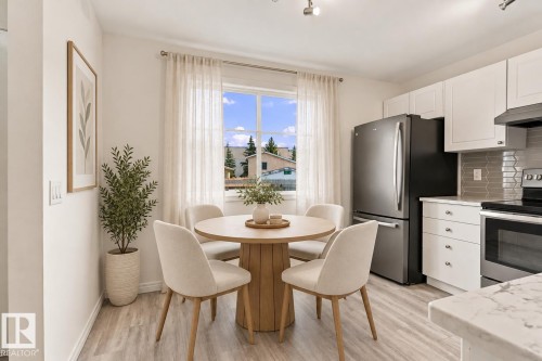 Bright kitchen space featuring white cabinetry, stainless steel appliances, a tiled backsplash, wood-finish flooring, and ample natural light - #3 18010 98 Av Nw, Edmonton, AB 