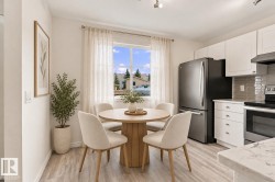 Bright kitchen space featuring white cabinetry, stainless steel appliances, a tiled backsplash, wood-finish flooring, and ample natural light - 
