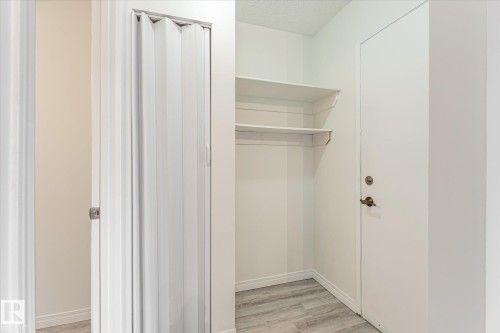 White accordion closet door, built-in shelving, white door with hardware, and wood-finish flooring - #3 18010 98 Av Nw, Edmonton, AB 