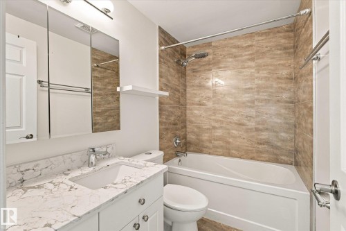 Bathroom featuring a white vanity with a stone countertop, built-in medicine cabinet, and a shower-over-tub with full-height tile surround - #3 18010 98 Av Nw, Edmonton, AB 