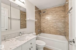 Bathroom featuring a white vanity with a stone countertop, built-in medicine cabinet, and a shower-over-tub with full-height tile surround - 