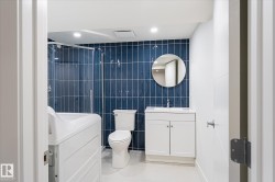 Bathroom featuring a walk-in shower with glass enclosure, white vanity, round wall mirror, and blue subway tile accent wall - 