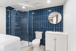 Glass-enclosed shower with blue tile surround, white vanity with integrated sink, modern circular mirror, and recessed lighting - 
