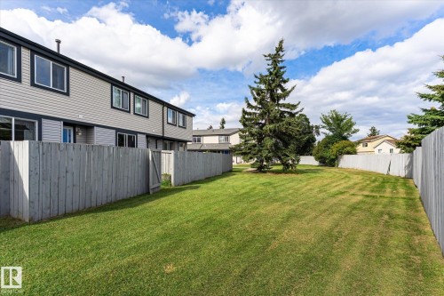 Expansive green space featuring manicured lawn and mature trees, bordered by a privacy fence and residential structures - #3 18010 98 Av Nw, Edmonton, AB 