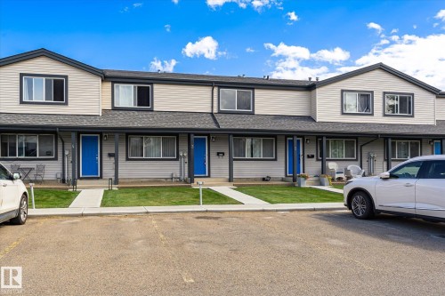 Multi-level townhome exterior featuring light-toned horizontal siding, dark trim, and blue entry doors - #3 18010 98 Av Nw, Edmonton, AB 