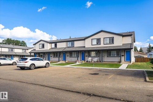Townhouse exterior featuring light-colored siding, contrasting dark trim, and vibrant blue entry doors - #3 18010 98 Av Nw, Edmonton, AB 
