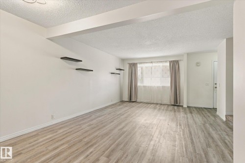 Spacious room featuring wood-finish flooring, light-toned walls, a large window, and built-in wall shelving - #3 18010 98 Av Nw, Edmonton, AB 