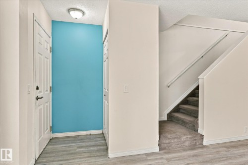 Foyer featuring wood-finish flooring, a paneled entry door, flush mount lighting, and a carpeted staircase with a handrail - #3 18010 98 Av Nw, Edmonton, AB 