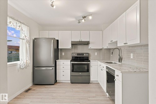White shaker-style cabinetry, stainless steel appliances, light-toned wood-finish flooring, and a subway tile backsplash - #3 18010 98 Av Nw, Edmonton, AB 