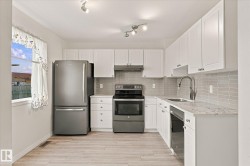 White shaker-style cabinetry, stainless steel appliances, light-toned wood-finish flooring, and a subway tile backsplash - 