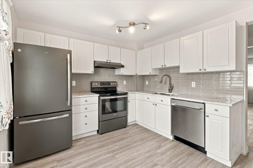 Kitchen featuring white shaker cabinetry, light-toned countertops, a full suite of appliances, a gray tile backsplash, and wood-finish flooring - #3 18010 98 Av Nw, Edmonton, AB 