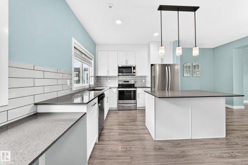 Kitchen featuring white cabinetry, gray countertops, stainless steel appliances, wood-finish flooring, and a kitchen island with pendant lighting - #56 804 Welsh Dr Sw, Edmonton, AB 