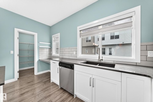 Kitchen featuring white shaker cabinetry, dark dual-basin sink, stainless steel dishwasher, and wood-finish flooring - #56 804 Welsh Dr Sw, Edmonton, AB 
