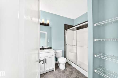 White vanity with a black faucet, sconce lighting, hexagon floor tiles, and a shower with a sliding glass door - #56 804 Welsh Dr Sw, Edmonton, AB 