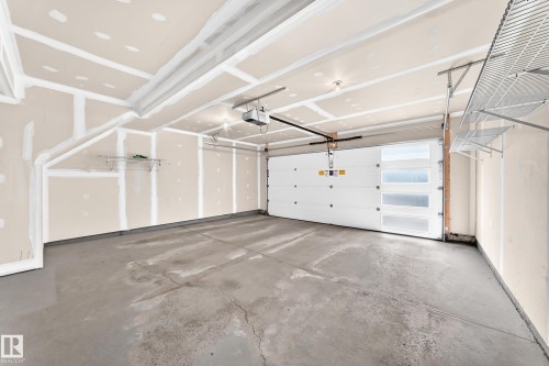 Concrete flooring, garage door opener, modern garage door with frosted glass panels, overhead wire shelving - #56 804 Welsh Dr Sw, Edmonton, AB 