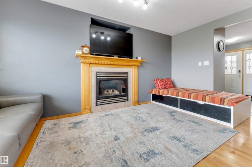 Hardwood flooring, fireplace with wood mantel, tiled fireplace surround, recessed television niche, and track lighting - 4510 164A Ave Nw, Edmonton, AB 