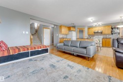 Open-concept living area with hardwood-finish flooring, a kitchen featuring wood cabinetry and light-colored countertops, and a staircase with wood banisters - 