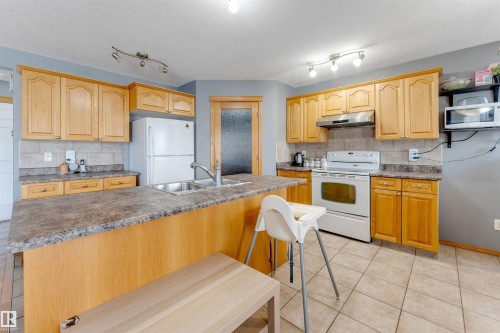 Kitchen featuring wood cabinetry, a center island with a double basin sink, tile flooring, and a tile backsplash - 4510 164A Ave Nw, Edmonton, AB 