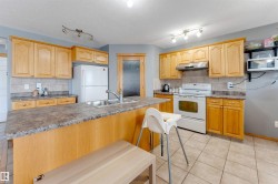 Kitchen featuring wood cabinetry, a center island with a double basin sink, tile flooring, and a tile backsplash - 