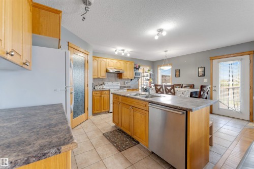 Spacious kitchen featuring warm wood cabinetry, stainless steel appliances, and a large center island with stone countertops - 4510 164A Ave Nw, Edmonton, AB 