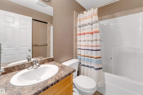 Bathroom featuring a vanity with an integrated sink, a neutral-toned countertop, a toilet, and a shower-tub combination with tile surround - 4510 164A Ave Nw, Edmonton, AB 