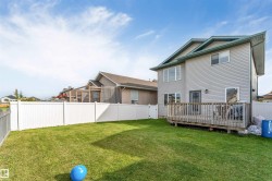 Expansive green lawn with a white privacy fence, multi-level vinyl siding exterior, and a wooden deck - 