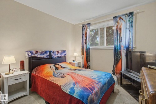 Carpeted bedroom featuring a window with drapes, a dark headboard, and light neutral wall paint - 8710 83 Avenue Nw, Edmonton, AB - Indoor Photo Showing Bedroom
