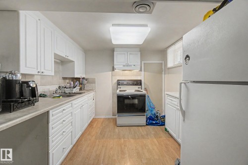 Kitchen featuring wood-finish flooring, white cabinetry, a light-toned countertop, and a tiled backsplash - 8710 83 Avenue Nw, Edmonton, AB - Indoor Photo Showing Kitchen
