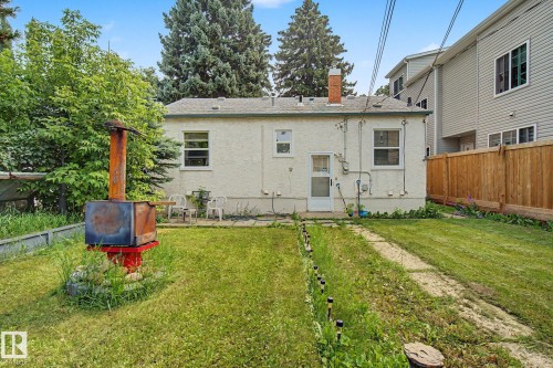 Rear exterior featuring a stucco finish, a red brick chimney, and a white back door - 8710 83 Avenue Nw, Edmonton, AB - Outdoor