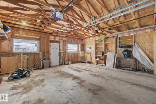 Spacious garage featuring exposed wood framing, a concrete floor, built-in shelving, two windows, and an interior access door - 8710 83 Avenue Nw, Edmonton, AB - Indoor
