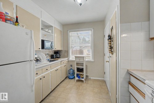 Galley kitchen featuring light-toned cabinetry, a window with blinds, and vinyl flooring - 8710 83 Avenue Nw, Edmonton, AB - Indoor Photo Showing Kitchen