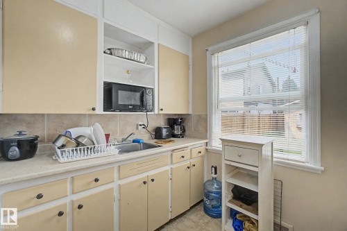 Kitchen featuring light-toned cabinetry with dark hardware, a single basin sink, and a tiled backsplash - 8710 83 Avenue Nw, Edmonton, AB - Indoor
